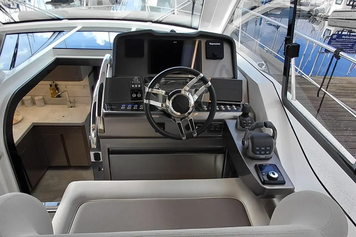 Modern yacht interior showing the steering wheel, control panel, and kitchenette with a sink and marble countertop.